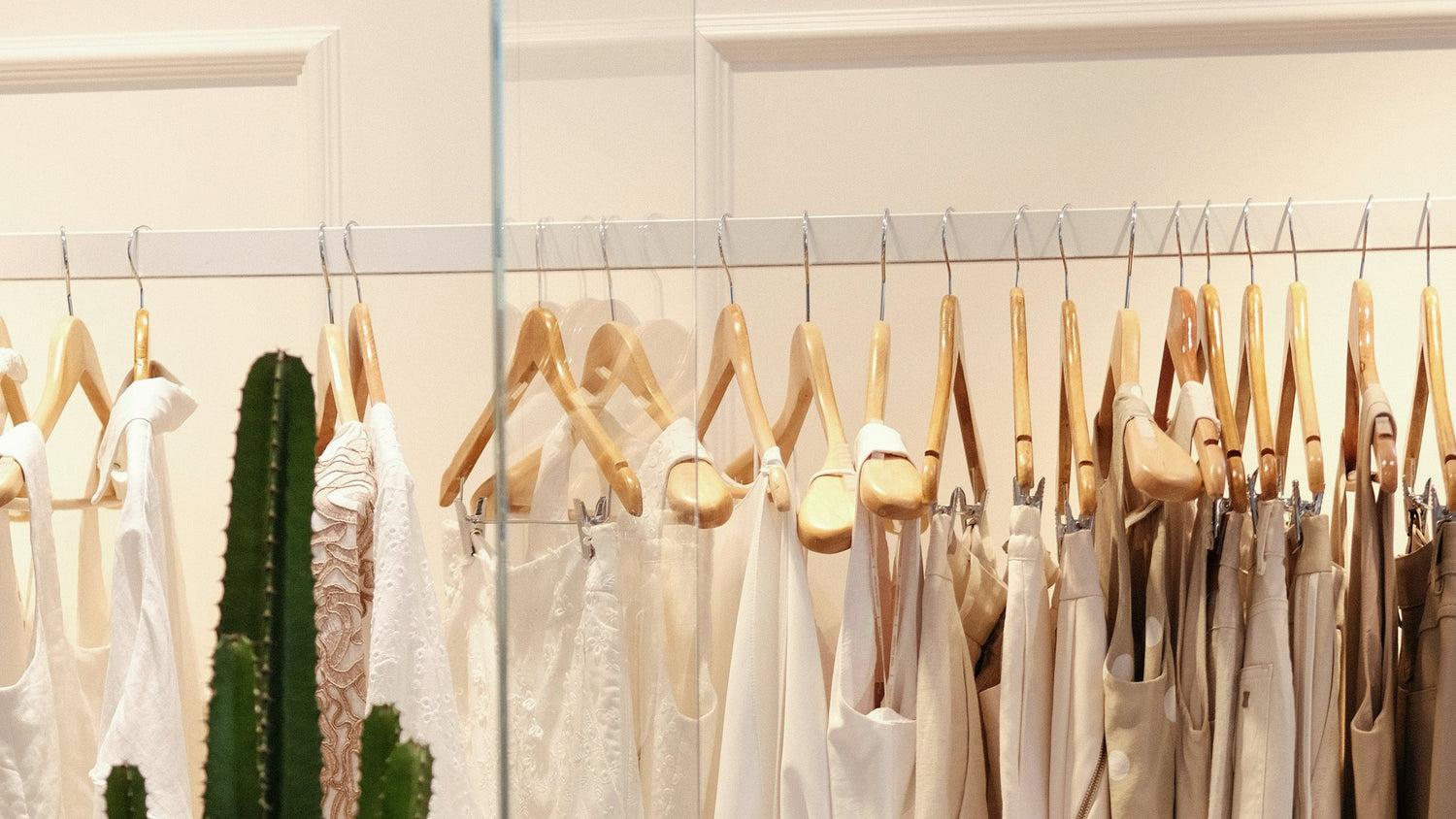 Cream and white clothes on wooden hangers, with a cactus in the foreground